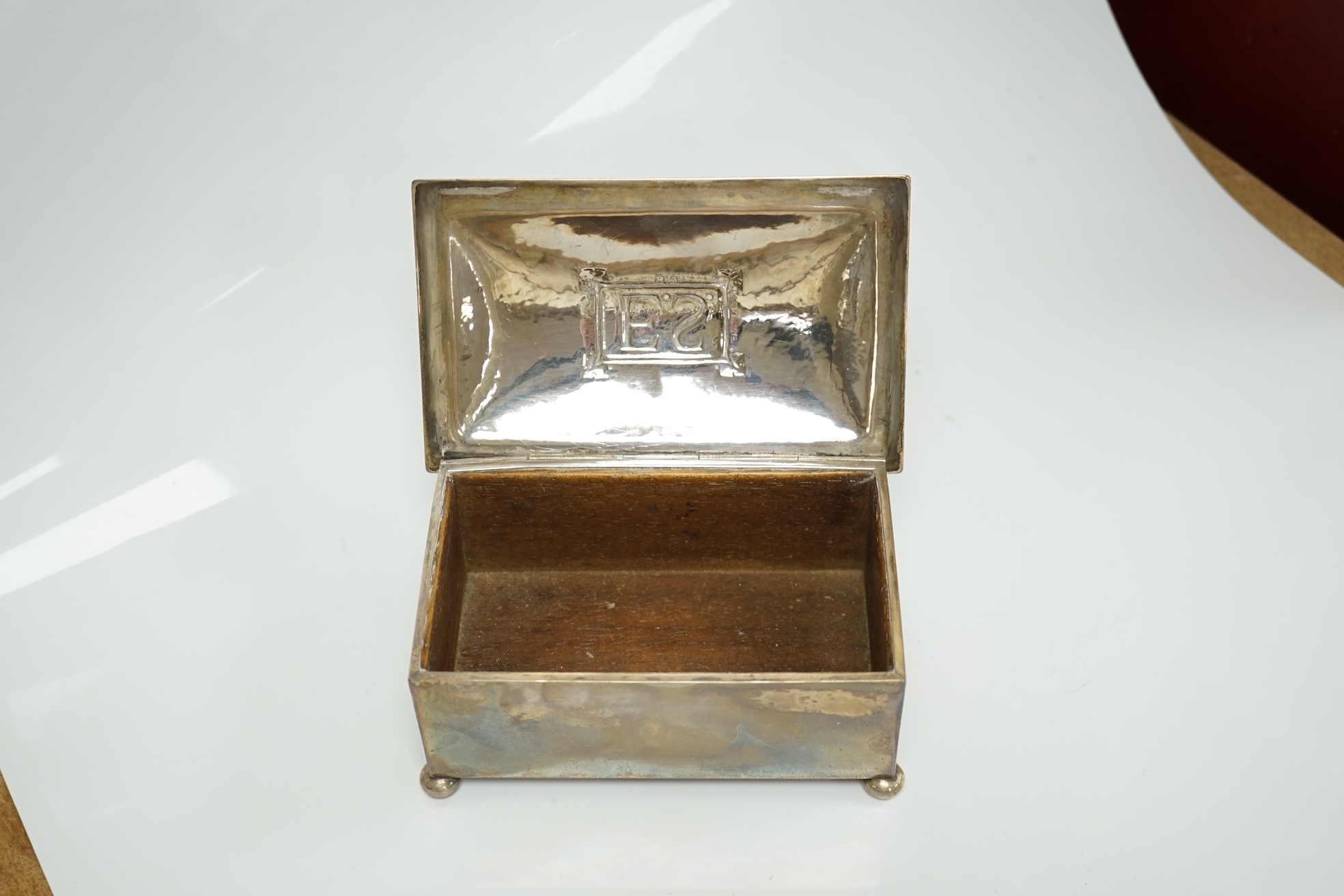 A George V Arts & Crafts silver mounted rectangular cigarette box, by Dryad Metal Works, Birmingham, 1924, on ball feet, the cover initialled ES, 15.2cm. Condition - fair